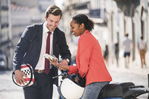 Glückliches junges Geschäftspaar mit Mobiltelefon und Motorroller in der Stadt, Lissabon, Portugal, lizenzfreies Stockfoto