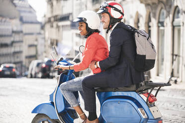 Happy young business couple riding motor scooter in the city, Lisbon, Portugal - UUF20117