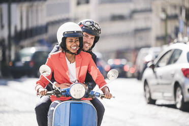 Happy young business couple riding motor scooter in the city, Lisbon, Portugal - UUF20119