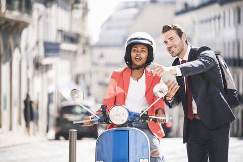 Geschäftsmann mit Mobiltelefon im Gespräch mit Frau auf Motorroller in der Stadt, Lissabon, Portugal, lizenzfreies Stockfoto