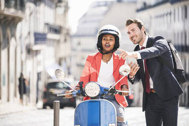 Geschäftsmann mit Mobiltelefon im Gespräch mit Frau auf Motorroller in der Stadt, Lissabon, Portugal - UUF20120