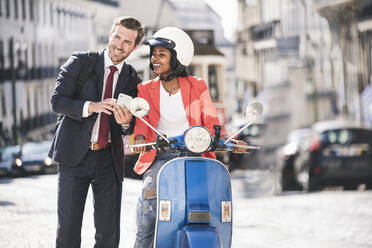 Glückliches junges Geschäftspaar mit Mobiltelefon und Motorroller in der Stadt, Lissabon, Portugal - UUF20121