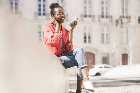 Smiling young woman with earphones and smartphone in the city, Lisbon, Portugal stock photo
