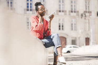 Lächelnde junge Frau mit Kopfhörern und Smartphone in der Stadt, Lissabon, Portugal - UUF20123