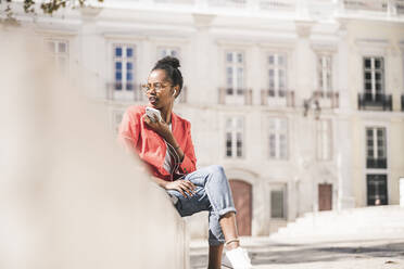 Junge Frau mit Kopfhörern und Smartphone in der Stadt, Lissabon, Portugal - UUF20128