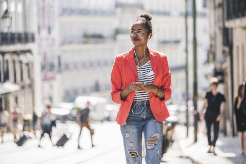 Young woman with earphones and smartphone looking around in the city, Lisbon, Portugal stock photo