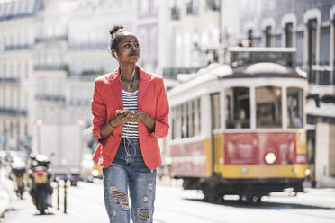 Young woman with earphones and smartphone looking around in the city, Lisbon, Portugal - UUF20132