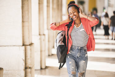 Happy young woman with headphones listening to music in the city, Lisbon, Portugal - UUF20137