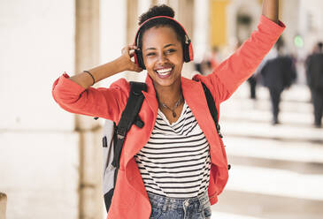 Portrait of happy young woman with headphones listening to music in the city, Lisbon, Portugal - UUF20139