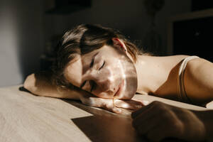 Porträt einer jungen Frau mit geschlossenen Augen, die sich bei Sonnenlicht an einen Holztisch lehnt - TCEF00035
