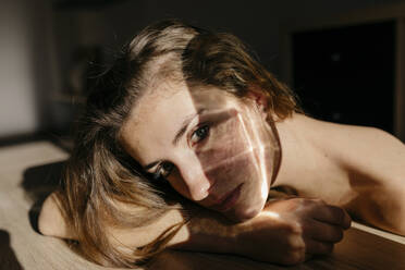 Porträt einer jungen Frau, die sich bei Sonnenlicht an einen Holztisch lehnt - TCEF00038