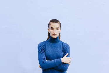 Porträt einer jungen Frau mit blauem Rollkragenpullover vor einer hellblauen Wand - TCEF00040