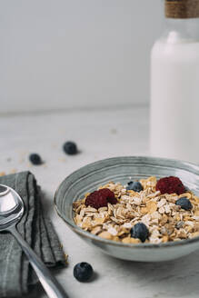 Schüssel mit Müsli mit Blaubeeren und Himbeeren und einer Flasche Joghurt im Hintergrund - JMHMF00033