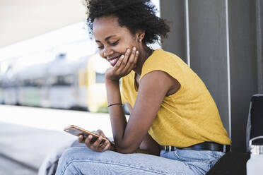 Smiling young woman using cell phone at the train station - UUF20146