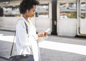 Junge Frau mit Mobiltelefon und Kopfhörern am Bahnhof - UUF20160