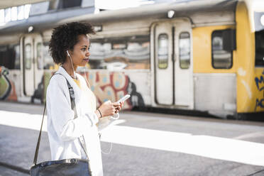 Junge Frau mit Mobiltelefon und Kopfhörern am Bahnhof - UUF20161