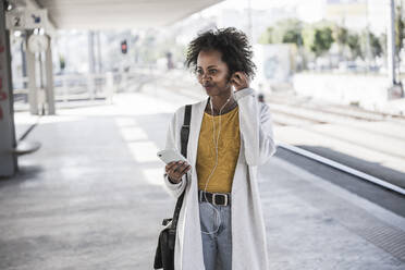 Junge Frau mit Mobiltelefon und Kopfhörern am Bahnhof - UUF20163