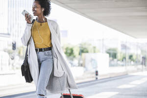 Lächelnde junge Frau, die unterwegs am Bahnhof ihr Smartphone benutzt - UUF20167