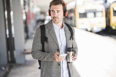 Junger Geschäftsmann mit Mobiltelefon und Kopfhörern am Bahnhof, lizenzfreies Stockfoto