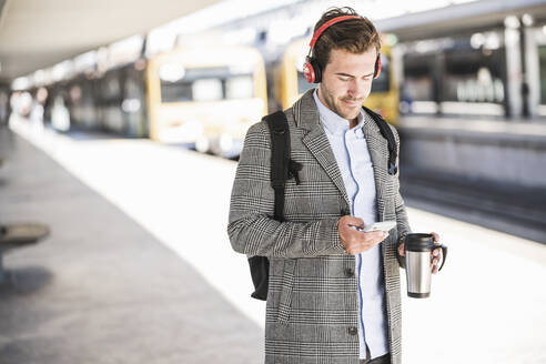 Young businessman with cell phone and headphones at the train station - UUF20175