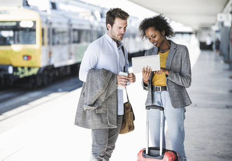 Junger Geschäftsmann und Geschäftsfrau benutzen gemeinsam ein Tablet am Bahnhof, lizenzfreies Stockfoto