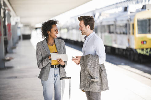 Young businessman and happy businesswoman using tablet together at the train station - UUF20182