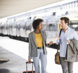 Junger Geschäftsmann und Geschäftsfrau benutzen gemeinsam ein Tablet am Bahnhof - UUF20187