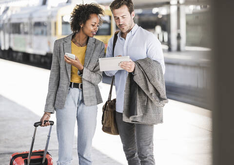 Junger Geschäftsmann und Geschäftsfrau benutzen gemeinsam ein Tablet am Bahnhof, lizenzfreies Stockfoto