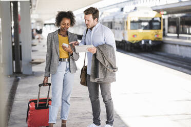 Junger Geschäftsmann und Geschäftsfrau nutzen Tablet und Smartphone am Bahnhof - UUF20190