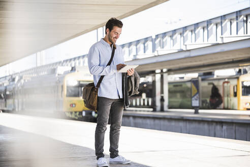 Casual young businessman using tablet at the train station - UUF20197