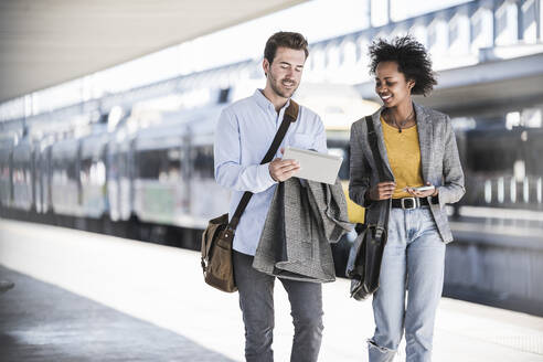 Junger Geschäftsmann und Geschäftsfrau benutzen gemeinsam ein Tablet am Bahnhof - UUF20199