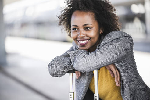 Portrait of smiling young businesswoman with suitcase at the train station - UUF20202