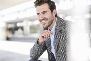 Porträt eines lächelnden jungen Geschäftsmannes auf dem Bahnhof - UUF20210