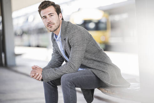 Portrait of young businessman sitting at the train station - UUF20212