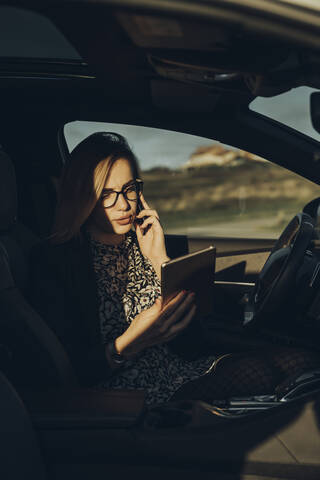 Junge blonde Frau benutzt Smartphone und Tablet im Auto, lizenzfreies Stockfoto