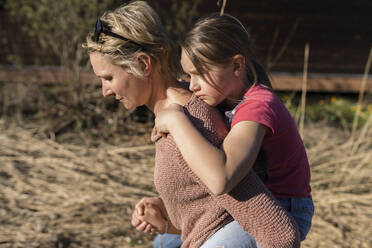 Mother walking in nature, carrying daughter piggyback - PSIF00353