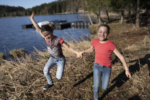 Schwestern haben Spaß am See, halten sich an der Hand, rennen und springen - PSIF00354