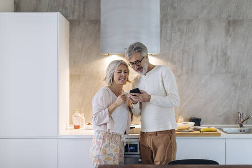 Älteres Paar benutzt Handy in der Küche zu Hause - SODF00505