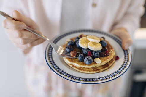 Close-up of woman holding a plate with pancakes and fruit - SODF00531