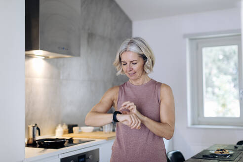 Ältere Frau benutzt Smartwatch in der Küche zu Hause - SODF00537