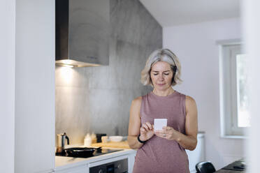 Reife Frau benutzt Mobiltelefon in der Küche zu Hause - SODF00538