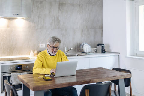 Mature man using laptop at table in kitchen at home stock photo