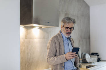 Reifer Mann benutzt Mobiltelefon in der Küche zu Hause - SODF00548