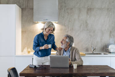 Happy mature couple with laptop on kitchen table at home - SODF00551