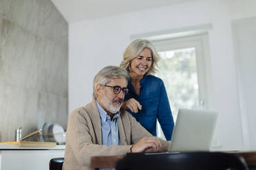 Älterer Mann mit Frau benutzt Laptop auf Küchentisch zu Hause - SODF00554