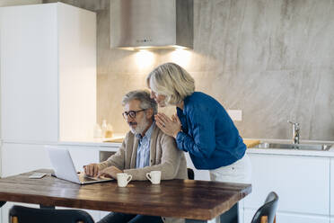 Älterer Mann mit Frau benutzt Laptop auf Küchentisch zu Hause - SODF00558