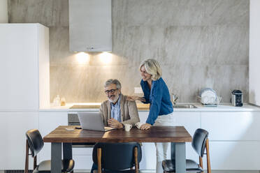 Mature man with wife using laptop on kitchen table at home - SODF00559