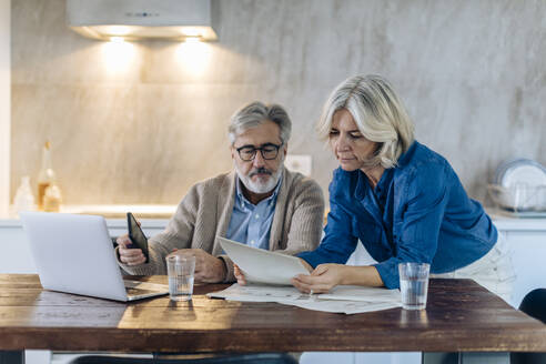 Mature couple with papers and laptop on kitchen table at home - SODF00561