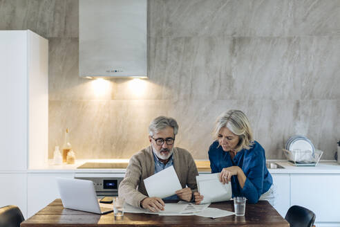 Älteres Paar mit Papieren und Laptop auf dem Küchentisch zu Hause - SODF00565