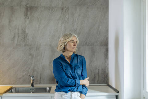 Porträt einer nachdenklichen reifen Frau in der Küche zu Hause, lizenzfreies Stockfoto